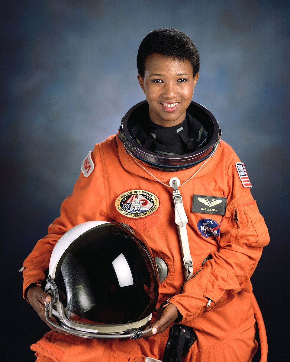 Mae Jemison in an orange flight suit, holding her helmet