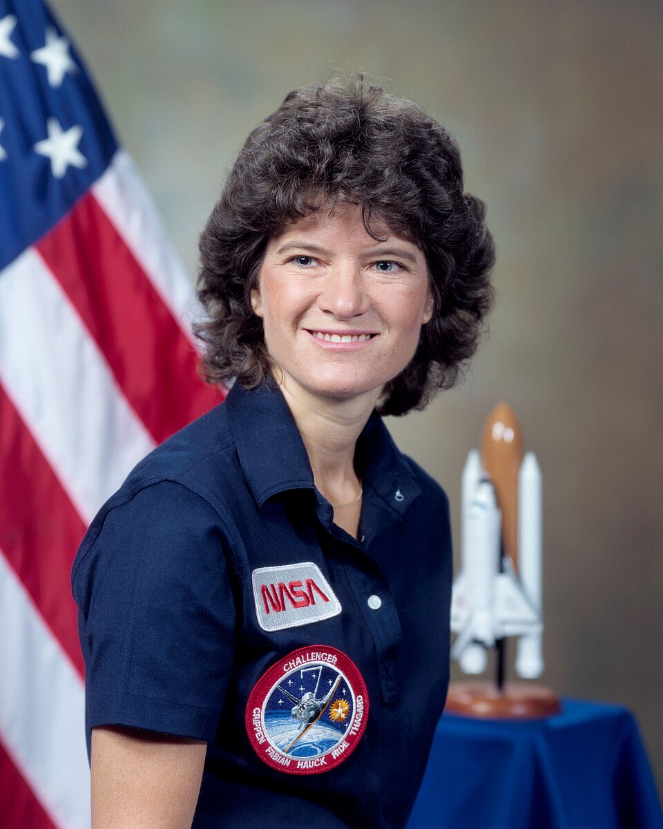 Sally Ride in a NASA flight jacket beside a Space Shuttle model