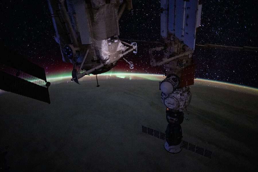 Station modules silhouetted against a green aurora over Earth's limb